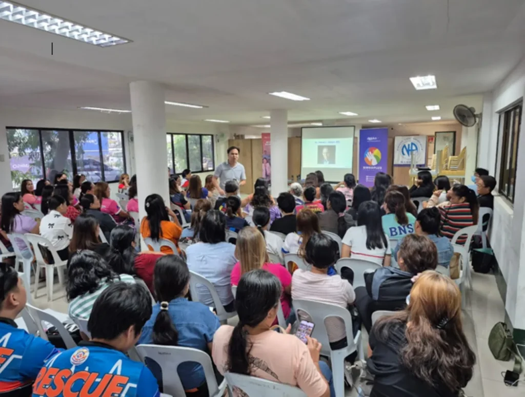Speaker addresses a packed room of attendees at a mental health training beside a BingoPlus Foundation banner