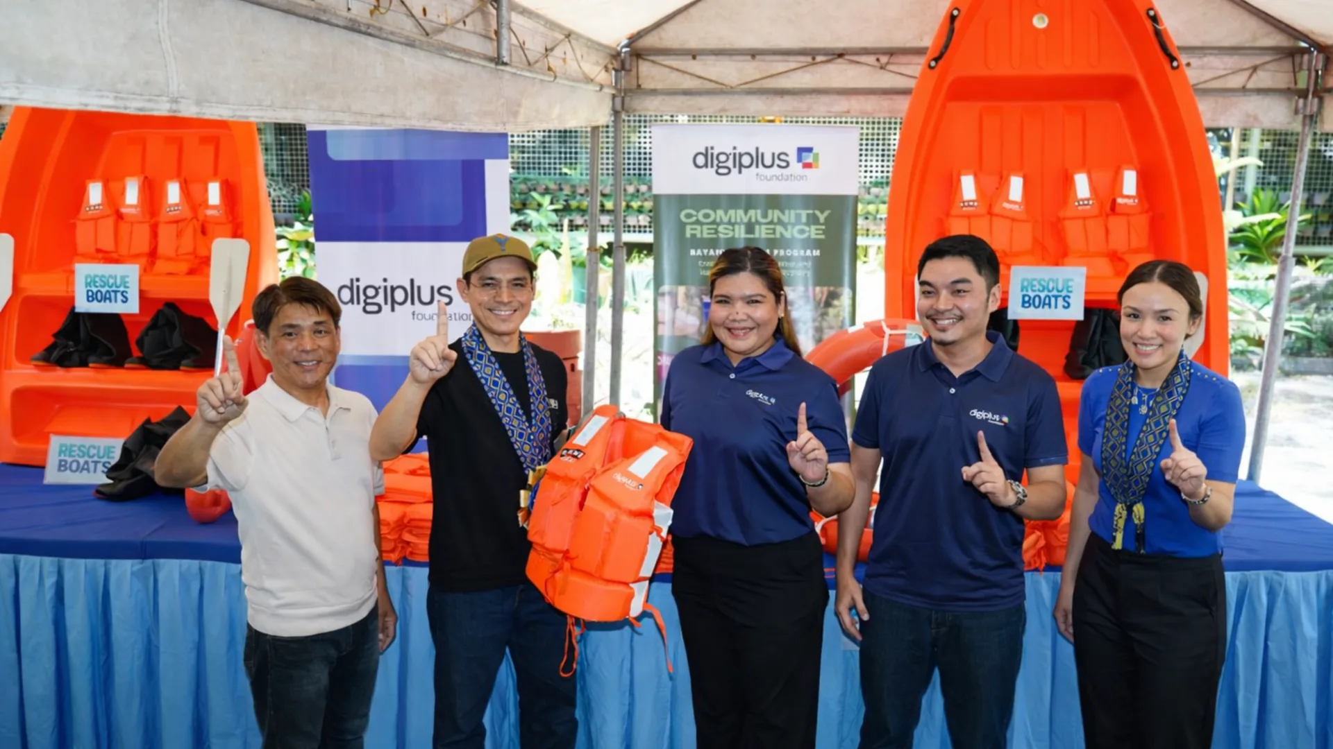 DigiPlus Foundation and partners pose with a life vest in front of orange rescue boats at a Community Resilience turnover