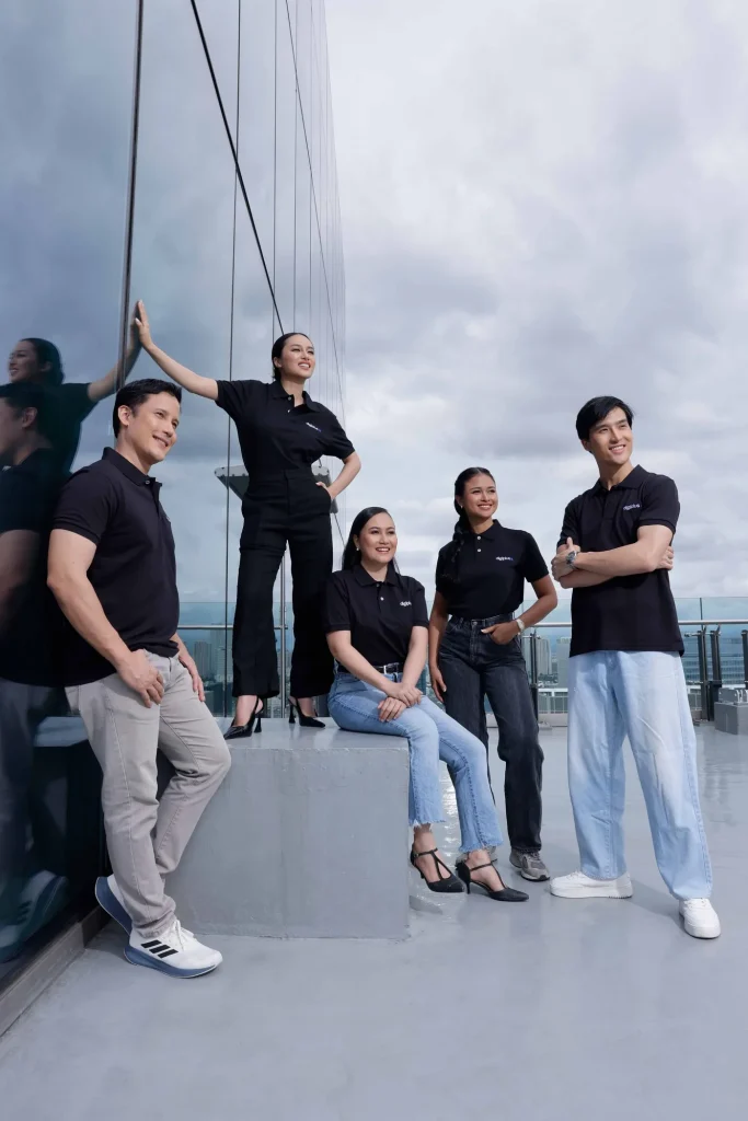 Five DigiPlus team members in black polo shirts posing on a rooftop beside a glass facade